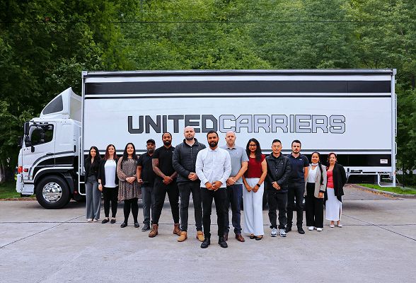 Group of twelve diverse people standing in front of a Kristotrans truck outdoors.